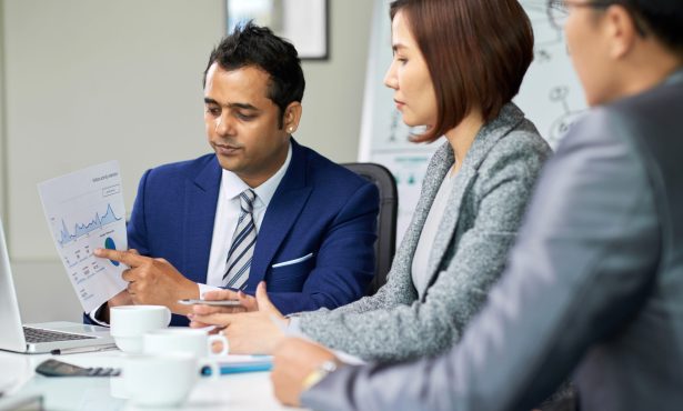 Businessman holding document with different diagrams and explaining its meaning to his partners during a meeting